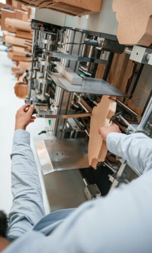 Operating printing cutting machine. Print house worker in white clothes is indoors.